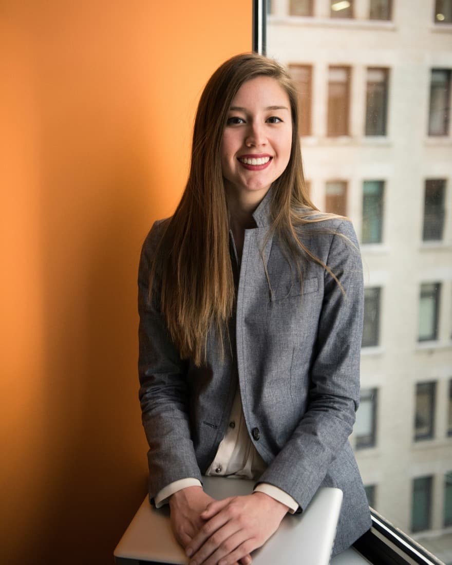 A smiling professional holding a laptop by an office window